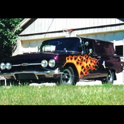 A purple truck with flames on it parked in front of a garage.