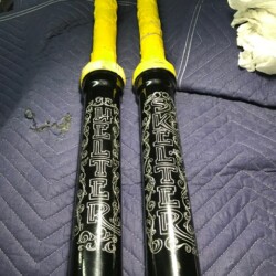 Two black and yellow baseball bats on a bed.