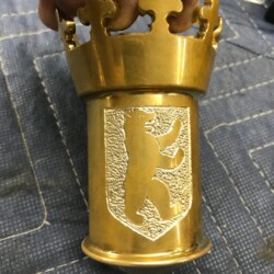 A person is holding a brass cup with a crown on it.